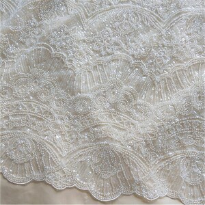 May include: White beaded fabric with a delicate, intricate pattern. The fabric has a subtle sheen and a soft, flowing texture.