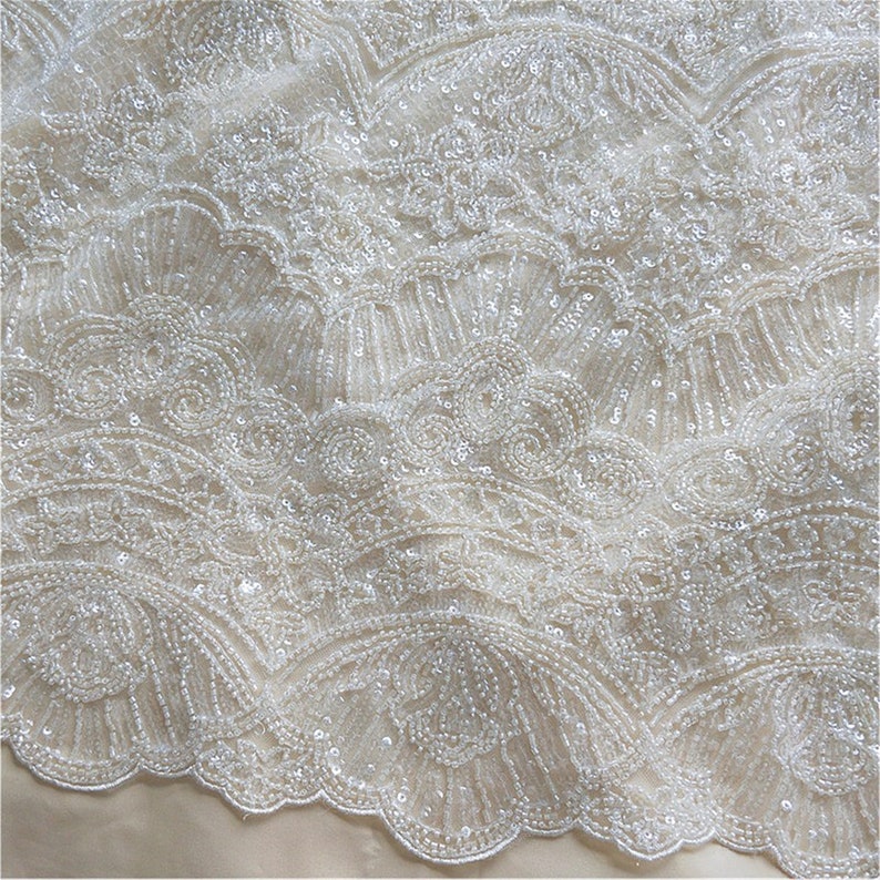 May include: White beaded fabric with a delicate, intricate pattern. The fabric has a subtle sheen and a soft, flowing texture.