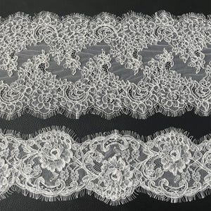 Op de afbeelding: Twee stroken witte kant met ingewikkelde bloemen- en krulpatronen. Het kant heeft geschulpte randen en een delicaat, open weefselontwerp, perfect voor knutselen of versieringen. Het kant is ideaal voor bruidskleding of andere speciale gelegenheidsprojecten.