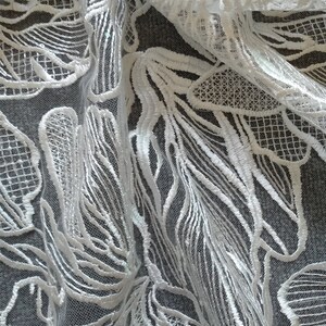 May include: White lace fabric with a delicate floral pattern. The lace is sheer and has a soft, flowing texture.