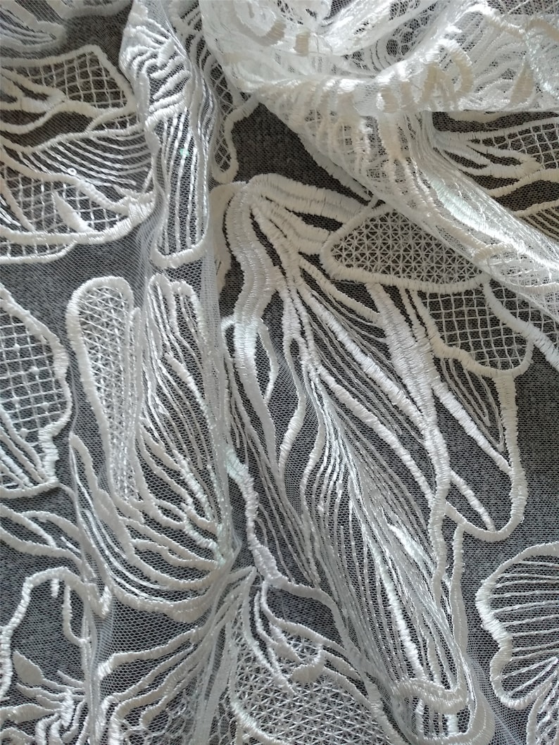 May include: White lace fabric with a delicate floral pattern. The lace is sheer and has a soft, flowing texture.