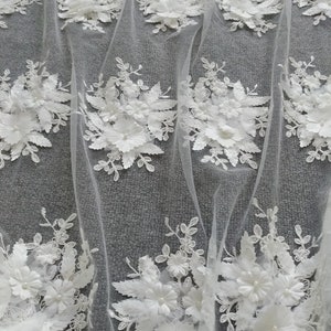 May include: White floral lace fabric with 3D flowers and leaves. The fabric is sheer and delicate, with a soft, romantic feel.