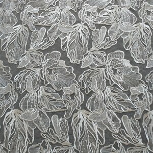 May include: White lace fabric with a floral pattern. The fabric is delicate and intricate, with a raised design.
