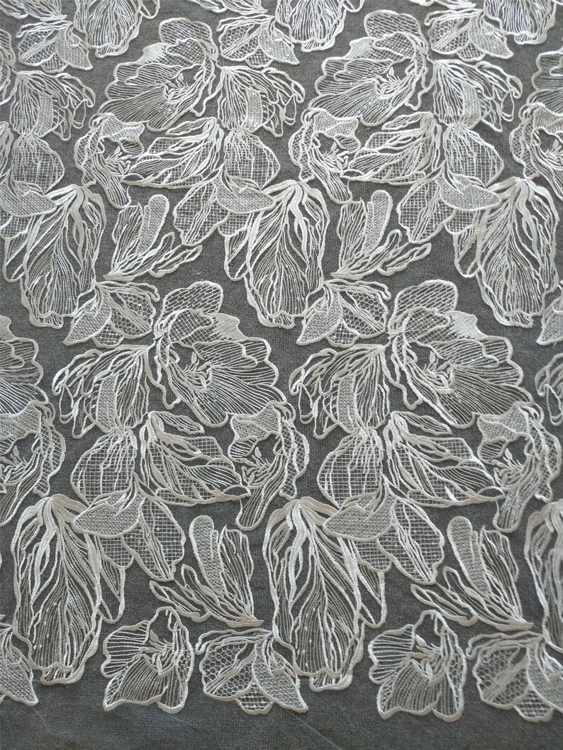 May include: White lace fabric with a floral pattern. The fabric is delicate and intricate, with a raised design.
