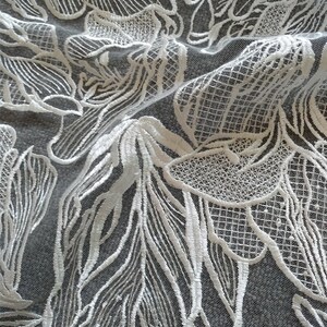 May include: White lace fabric with a floral pattern. The lace is delicate and intricate, with a fine mesh background.