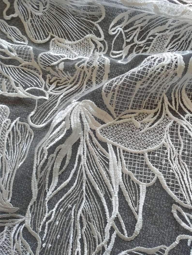 May include: White lace fabric with a floral pattern. The lace is delicate and intricate, with a fine mesh background.