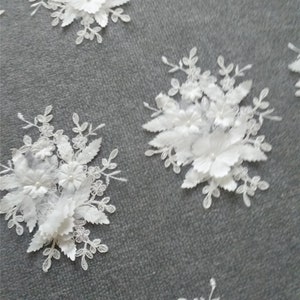 May include: White floral lace fabric with 3D flowers and leaves. The fabric has a delicate and intricate design with a mesh background.