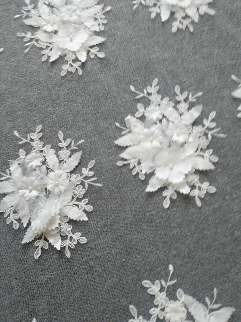 May include: White floral lace fabric with 3D flowers and leaves. The fabric has a delicate and intricate design with a mesh background.