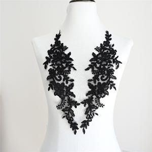 May include: Two black lace floral appliques. Each applique features a detailed design of flowers and leaves. The appliques are symmetrical and are displayed on a white mannequin. The lace has a delicate, intricate pattern.