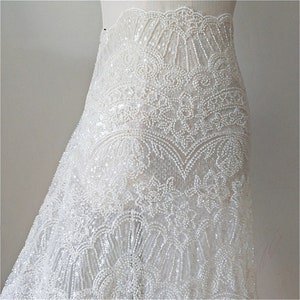 May include: White beaded lace fabric with a delicate floral pattern. The lace is sewn onto a sheer mesh backing.