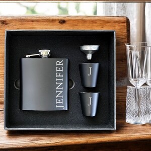 Könnte beinhalten: Eine schwarze Flasche mit der Gravur "JENNIFER", ein Trichter, zwei Schnapsgläser und ein klares Glas mit Diamantmuster. Die Artikel befinden sich in einer schwarzen Box mit schwarzem Innenraum.