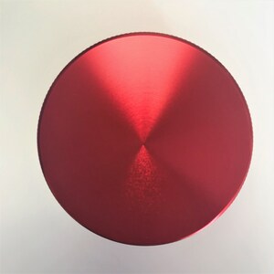 Puede incluir: Una tapa redonda de metal de color rojo brillante con un acabado cepillado brillante.