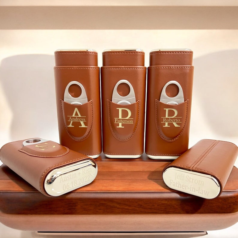 May include: Five brown leather cigar cases with silver accents and personalized engravings. Each case has a built-in cutter and a silver band with a name and date.
