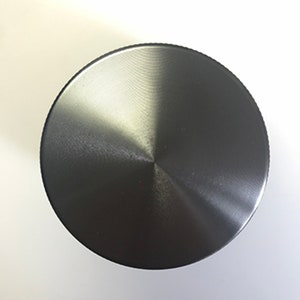 Puede incluir: Una tapa redonda de metal plateado con acabado cepillado.