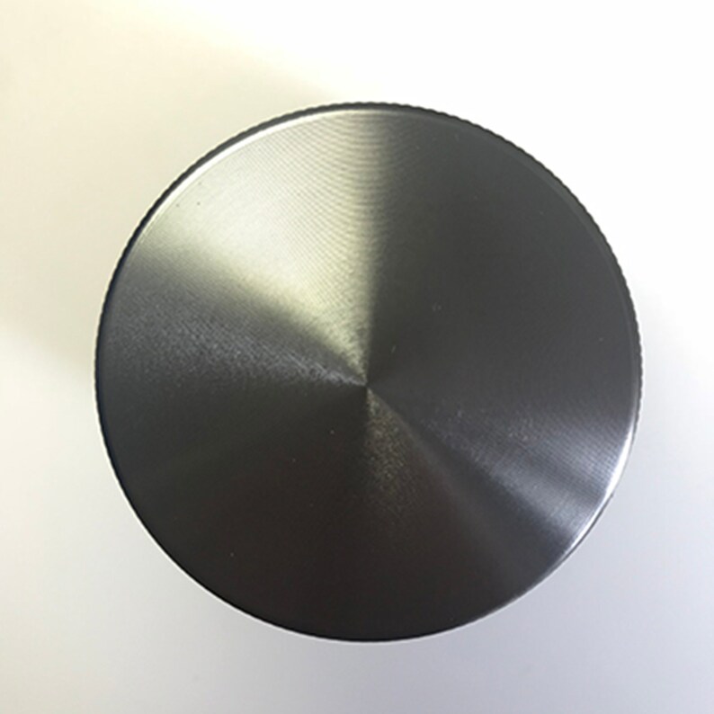 Puede incluir: Una tapa redonda de metal plateado con acabado cepillado.