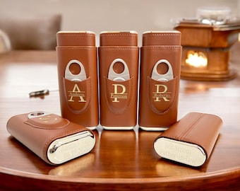 May include: Five brown leather cigar cases with silver accents. Each case has a personalized inscription and a built-in cutter. The inscriptions include names like "Andress", "Patterson", and "Roberto".