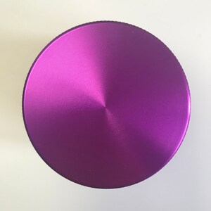 Puede incluir: Un molinillo de metal morado con una parte superior circular y un acabado cepillado.