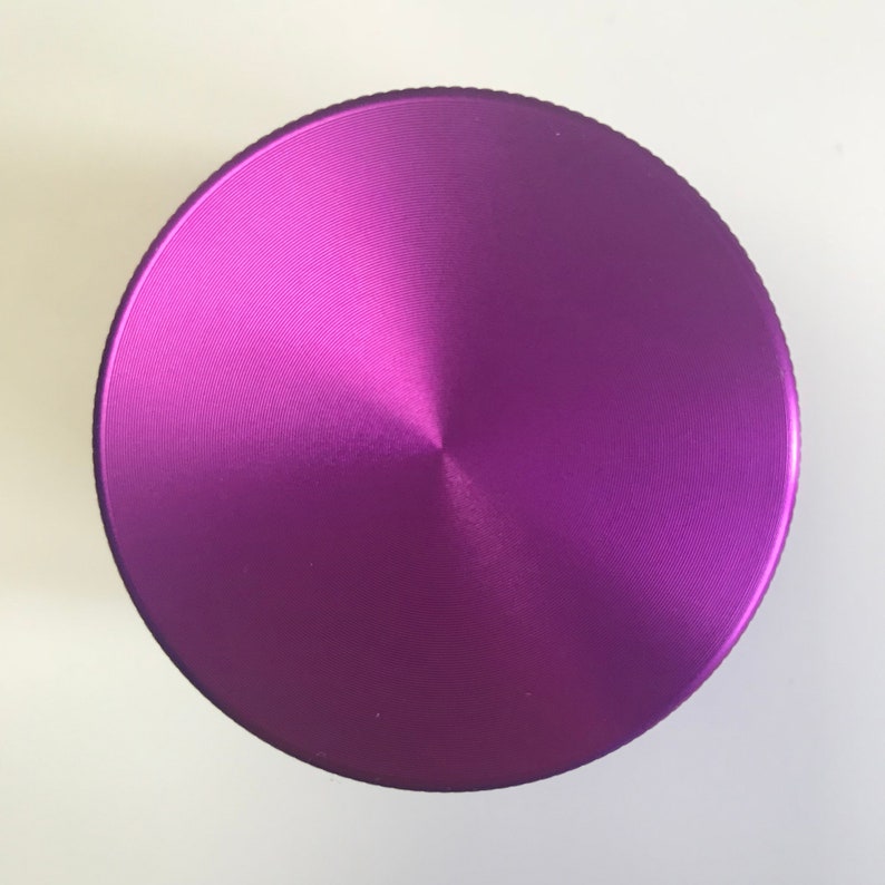 Puede incluir: Un molinillo de metal morado con una parte superior circular y un acabado cepillado.