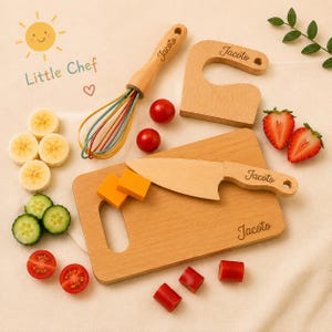 May include: A wooden toy kitchen set featuring a cutting board, a knife, a whisk, and a hook, all engraved with the name Jacoto. The set includes sliced banana, cucumber, tomato, and cheese pieces, with the text Little Chef and a sun icon.