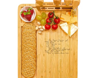 May include: A wooden cutting board with a handwritten recipe for "Claw Ground Classics" on the surface. The board has a built-in knife holder with four knives and a cheese knife. There are also crackers, cheese, grapes, and strawberries on the board.