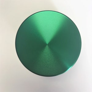 Puede incluir: Un molinillo de metal verde con una parte superior circular y una superficie texturizada.