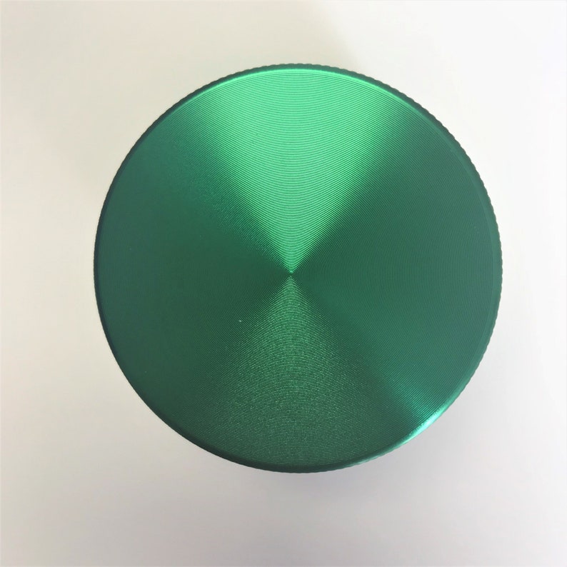Puede incluir: Un molinillo de metal verde con una parte superior circular y una superficie texturizada.