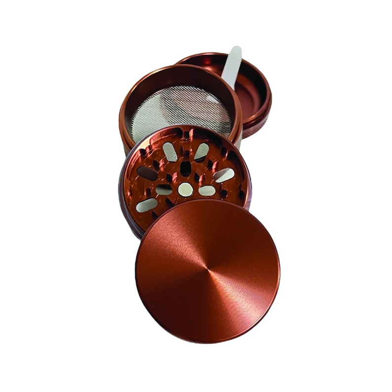 Puede incluir: Un molinillo de metal de color cobre de cuatro piezas con una pantalla y un raspador. El molinillo tiene una forma circular y un acabado cepillado.