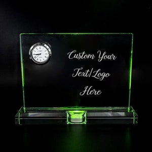 May include: A green glass plaque with a small clock and a space for custom text or a logo. The text "Custom Your Text/Logo Here" is engraved on the plaque. The plaque has a green light underneath.