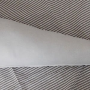 May include: A white, cone-shaped pillow with a rounded end. The pillow is lying on a striped fabric.