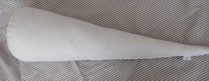 May include: A white, cone-shaped pillow with a rounded end. The pillow is lying on a striped fabric.