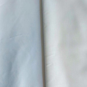 May include: Two pieces of white fabric, one slightly lighter than the other, are folded together. The fabric has a smooth, even texture.
