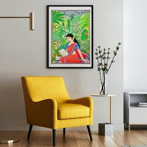 May include: A framed painting of a woman in a red and blue sari sitting in a lush green garden. She is reading a book and there is a crescent moon in the sky.