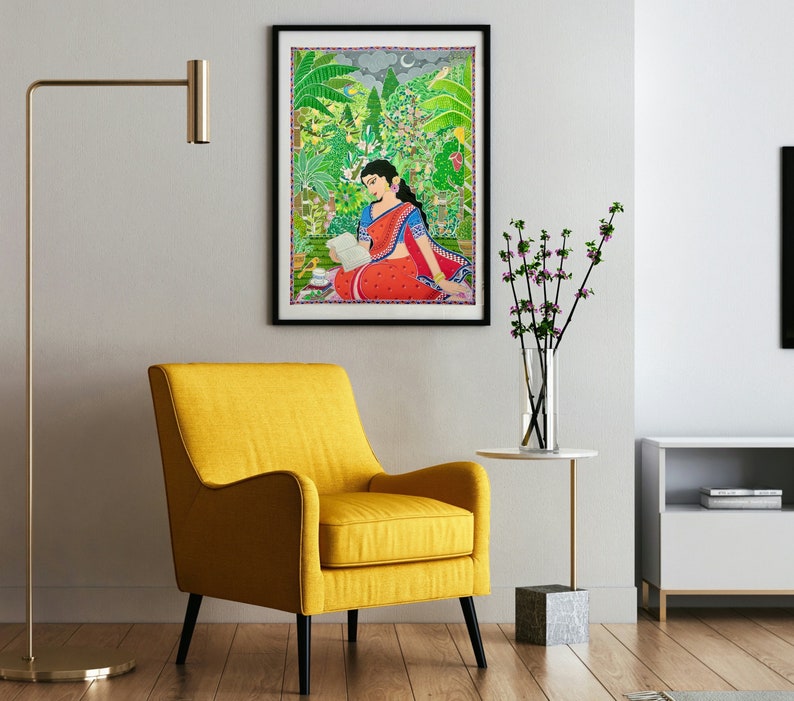 May include: A framed painting of a woman in a red and blue sari sitting in a lush green garden. She is reading a book and there is a crescent moon in the sky.