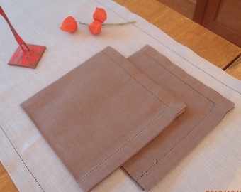 May include: Two brown linen napkins with a stitched border, folded and placed on a white linen tablecloth.