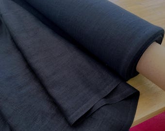 May include: A roll of solid black fabric with a visible woven texture. The material is tightly wound into a cylindrical shape, with a portion of the fabric unrolled and draped downwards, showcasing the consistent dark color and the weave pattern.