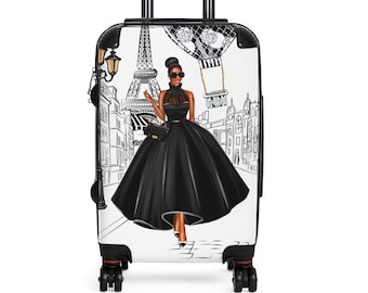 May include: A white suitcase with a black and white illustration of a woman in a black dress walking in front of the Eiffel Tower. The suitcase has a black handle and black wheels.