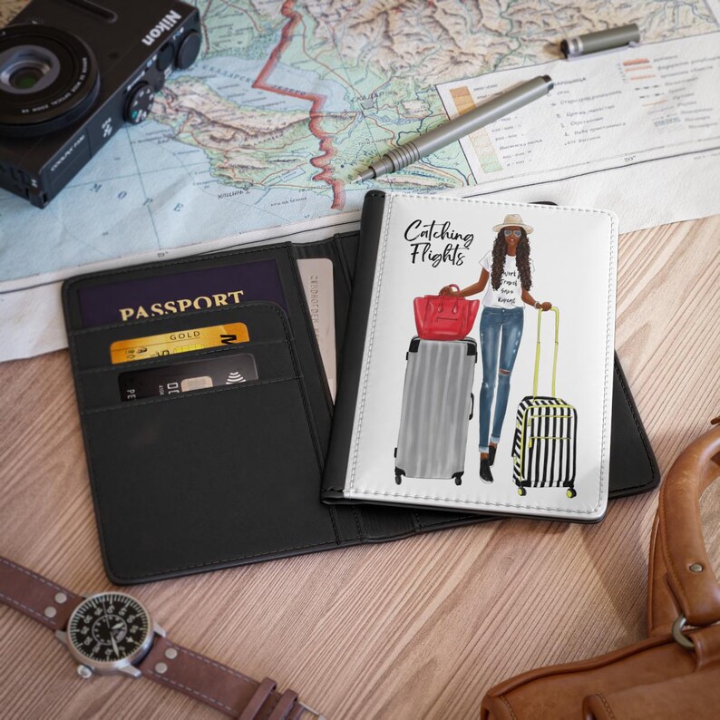 May include: Black passport holder with the word "PASSPORT" in white text. The holder has a pocket for cards and a clear plastic window for a photo. The holder is open to reveal a white passport cover with the text "Catching Flights" and an illustration of a woman with luggage.