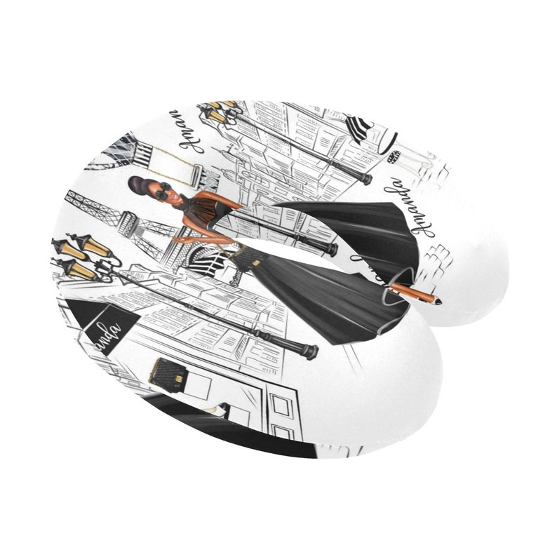 May include: A white travel neck pillow with a black and white illustration of a woman walking in Paris. The illustration includes the Eiffel Tower, street lamps, and the text "Bonjour" and "Avoir".