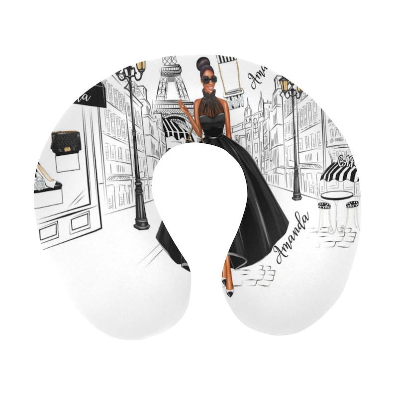 May include: A white travel neck pillow with a black and white illustration of a woman in a black dress walking in Paris. The Eiffel Tower is in the background. The text "Amanda" is written on the pillow.