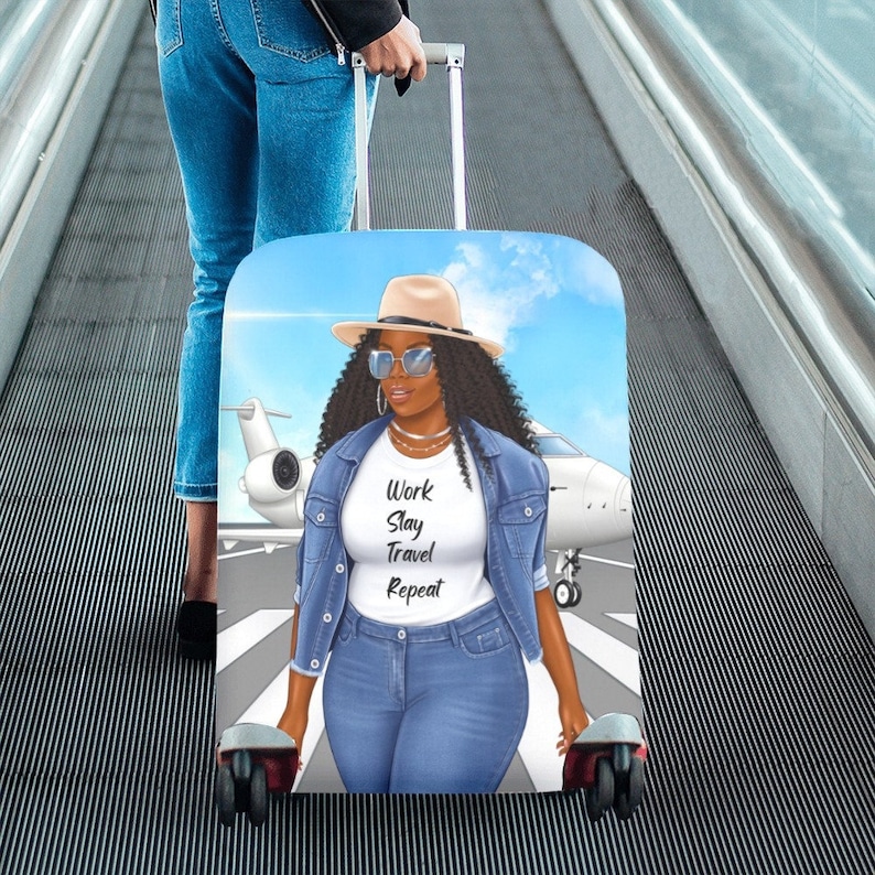 May include: A luggage cover featuring a cartoon illustration of a woman wearing a denim jacket, sunglasses, and a hat. The woman is standing in front of a private jet with the text "Work Slay Travel Repeat" on her shirt. The luggage cover is blue and white.