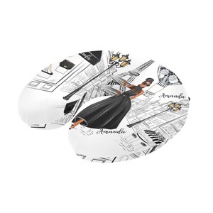 May include: A white travel neck pillow with a black and white illustration of a woman in a black dress walking in Paris. The illustration includes the Eiffel Tower, streetlights, and the text "Amanda".
