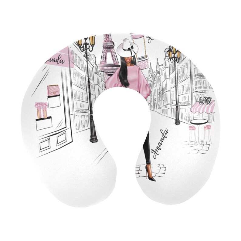 May include: A white travel pillow with a pink and black illustration of a woman in a pink sweater and black pants walking in Paris. The Eiffel Tower is in the background. The text "Amanda" is written on the pillow.