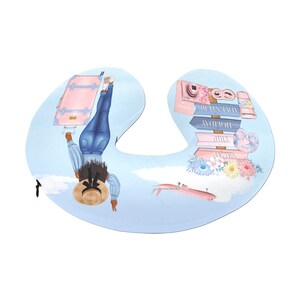May include: A blue and white travel themed neck pillow with a woman in a blue denim outfit and a straw hat holding a pink suitcase. The pillow has a floral design and a small airplane on the bottom. The text on the pillow reads "Vacay, Trip, Holiday, Adventure".