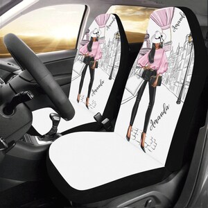 May include: Two black and white car seat covers with a white background and a black and white illustration of a woman in a pink shirt and black pants walking down a street. The woman is wearing a white hat and carrying a black purse. The text "Amanda" is written on each cover.