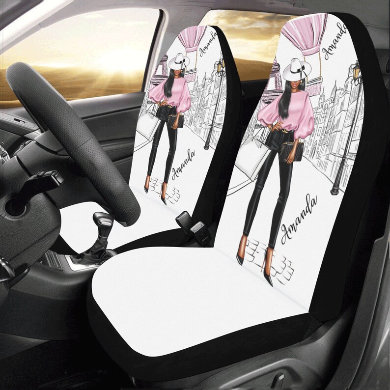May include: Two black and white car seat covers with a white background and a black and white illustration of a woman in a pink shirt and black pants walking down a street. The woman is wearing a white hat and carrying a black purse. The text "Amanda" is written on each cover.