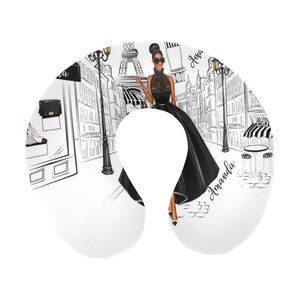 May include: A white travel neck pillow with a black and white illustration of a woman in a black dress walking in Paris. The Eiffel Tower is in the background. The text "Amanda" is written on the pillow.