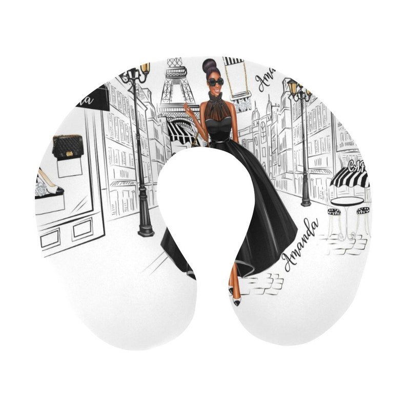 May include: A white travel neck pillow with a black and white illustration of a woman in a black dress walking in Paris. The Eiffel Tower is in the background. The text "Amanda" is written on the pillow.