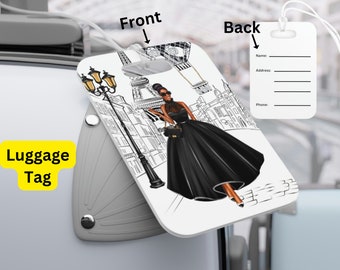 May include: A white luggage tag with a black and white illustration of a woman in a black dress walking in front of the Eiffel Tower. The back of the tag has spaces for a name, address, and phone number.