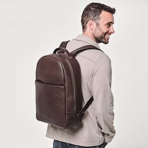 Può includere: Uno zaino in pelle marrone scuro caratterizzato da un design arrotondato, una grande tasca frontale e spallacci regolabili. La borsa include una maniglia superiore e cerniere in metallo sullo scomparto principale e sulla tasca frontale.