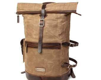 Könnte beinhalten: Ein brauner Canvas-Rucksack mit Lederriemen und Schnallen. Der Rucksack hat einen Rollverschluss und eine Fronttasche mit Reißverschluss. Der Markenname "TRAVELLER" ist auf der Vorderseite der Tasche sichtbar.